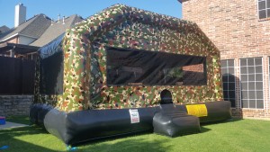 big camouflage bounce house on grass in a backyard