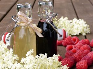 two-homemade-glass-bottle-syrups-raspberries-white-flowers