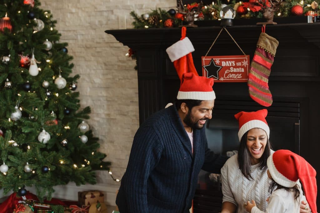 family around christmas tree wearing santa hats