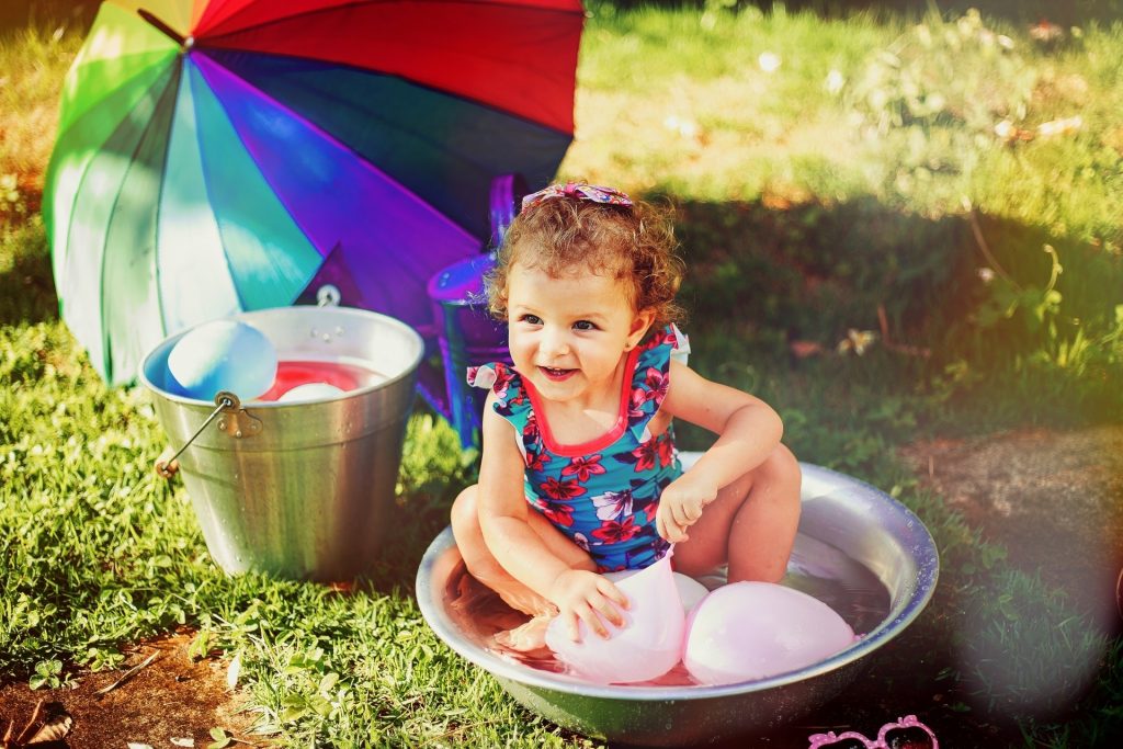little girl sitting in small pool with water balloons