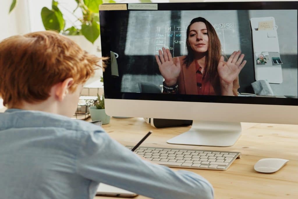 student boy sitting at desk on video call with teacher