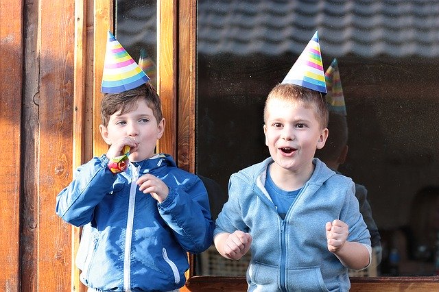 two kids boys standing in front of a window with party hats on
