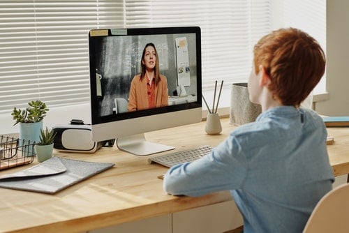 student sitting at a desk on a video call with a teacher