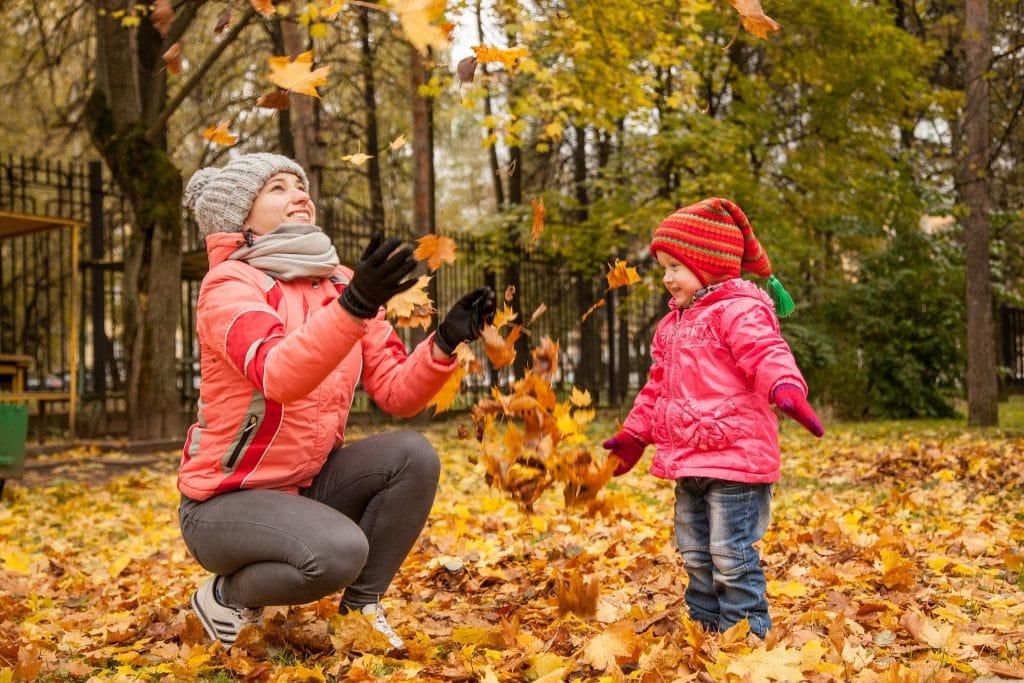 mom and little girl play in the fall leaves