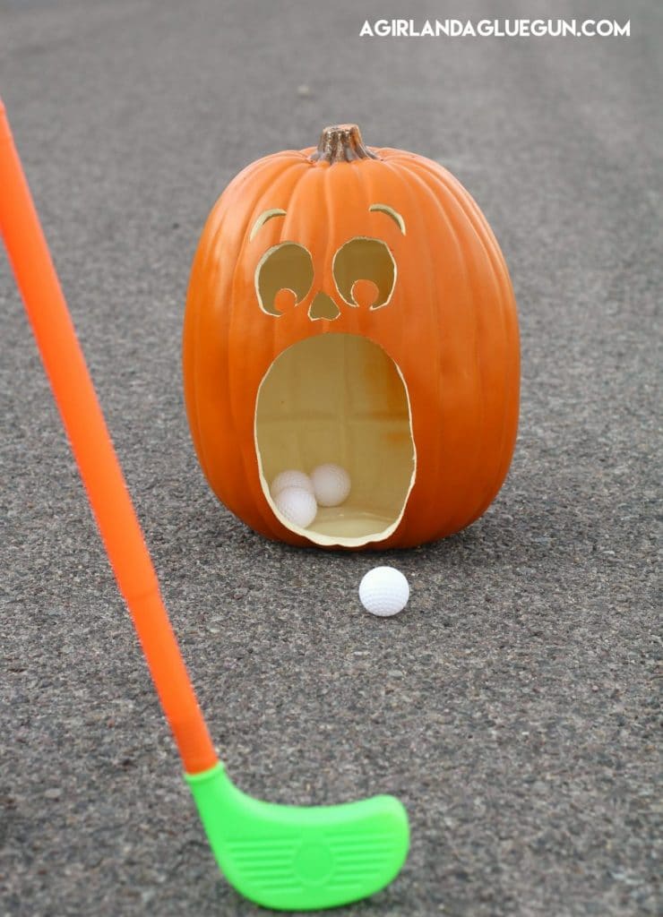 pumkin carved with open mouth and person golfing golf balls into the pumpkins mouth