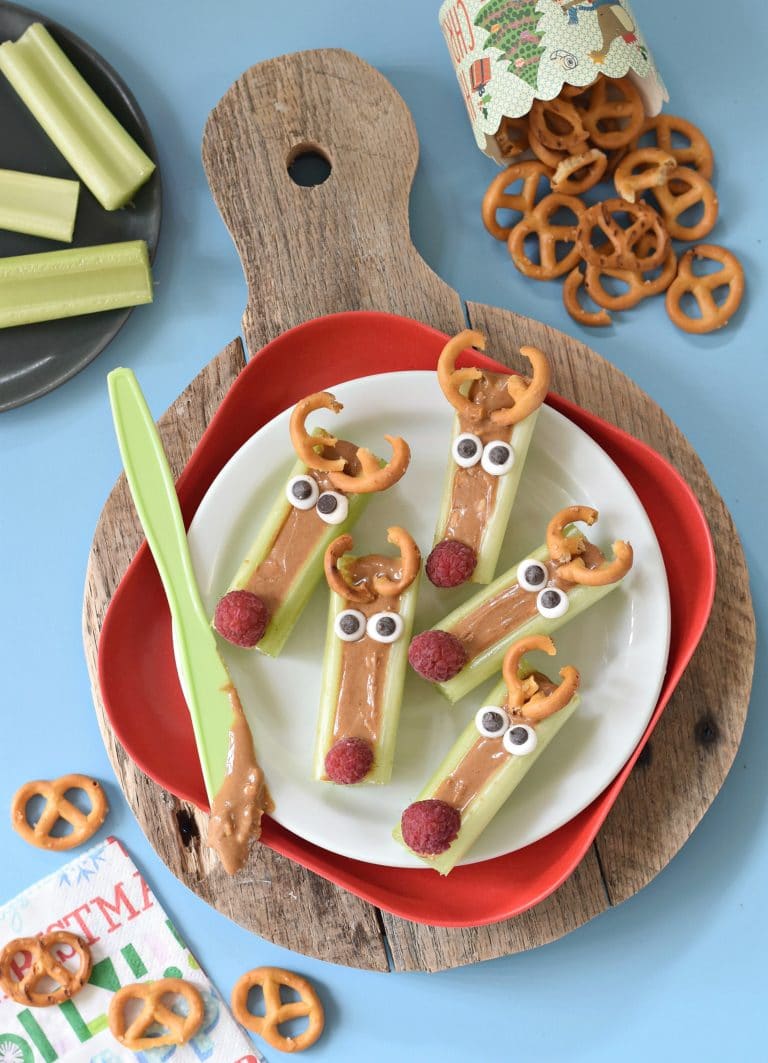 snacks made to resemble reindeer, celery filled with peanut butter with pretzel antlers, google eyes, and a raspberry nose