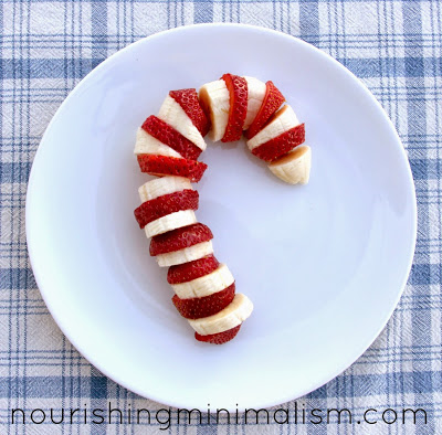 strawberry and banana pieces cut and assembled like a candy cane on a white plate on blue plaid table cloth