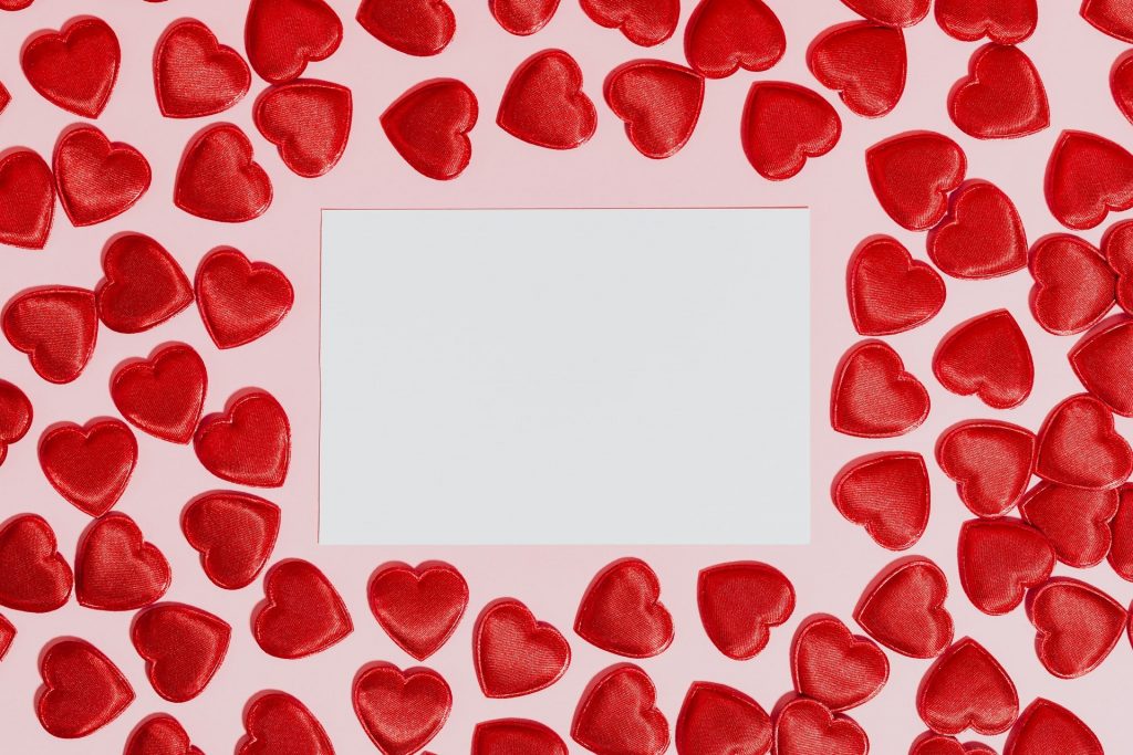 white blank piece of paper surrounded by re hearts on a pink background