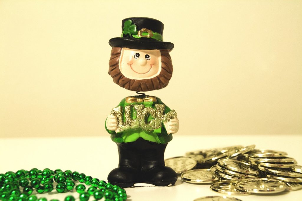 plastic toy leprechaun on a table next to a green bead necklace and gold coins