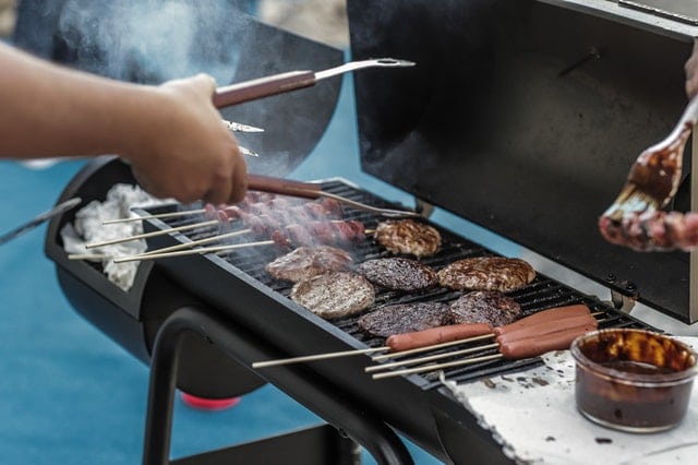 person holding grilling tongs while barbequing / grilling meat on grill outside