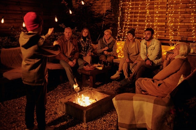 large family gathered outdoors in the backyard near a fire pit with lights on the fence