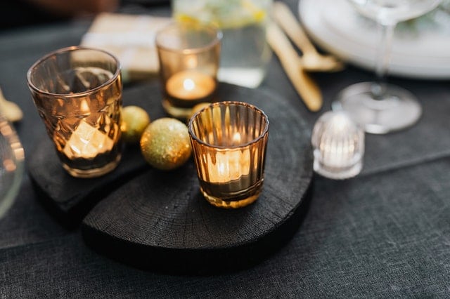 set of three candles lit on a black table around plate ware 