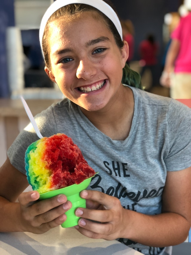 young girl smiling eating a rainbow snow cone 