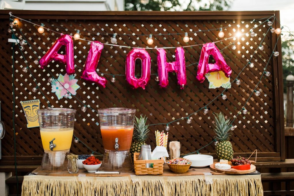 aloha party balloon outside over a party table with juices, drinks, food, and a luau theme