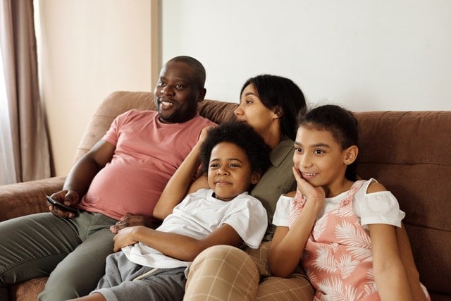 black family mom dad 2 kids sitting on the couch watching tv movie night