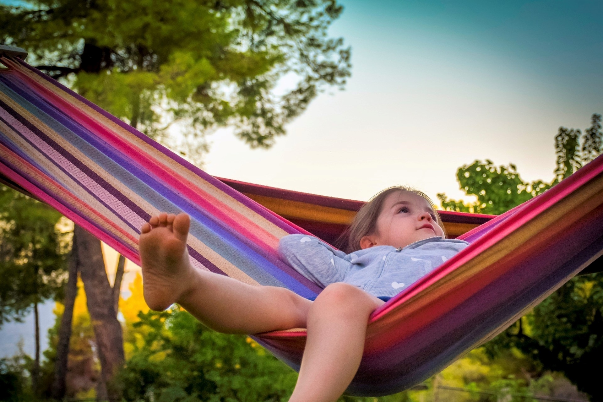 little kid sitting back on hammock outside in the backyard in summmer