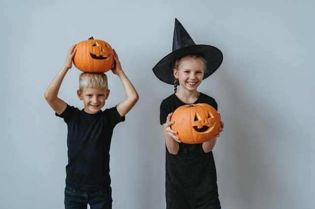 two kids dressed in black holding carved pumpkin jack-o-lanterns