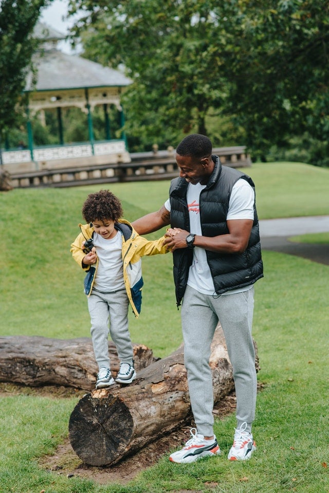 father and son playing in a park by a log