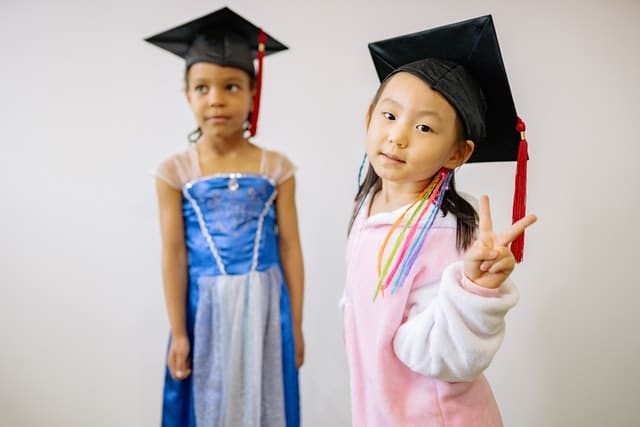 two little girls wearing dresses and graduation caps
