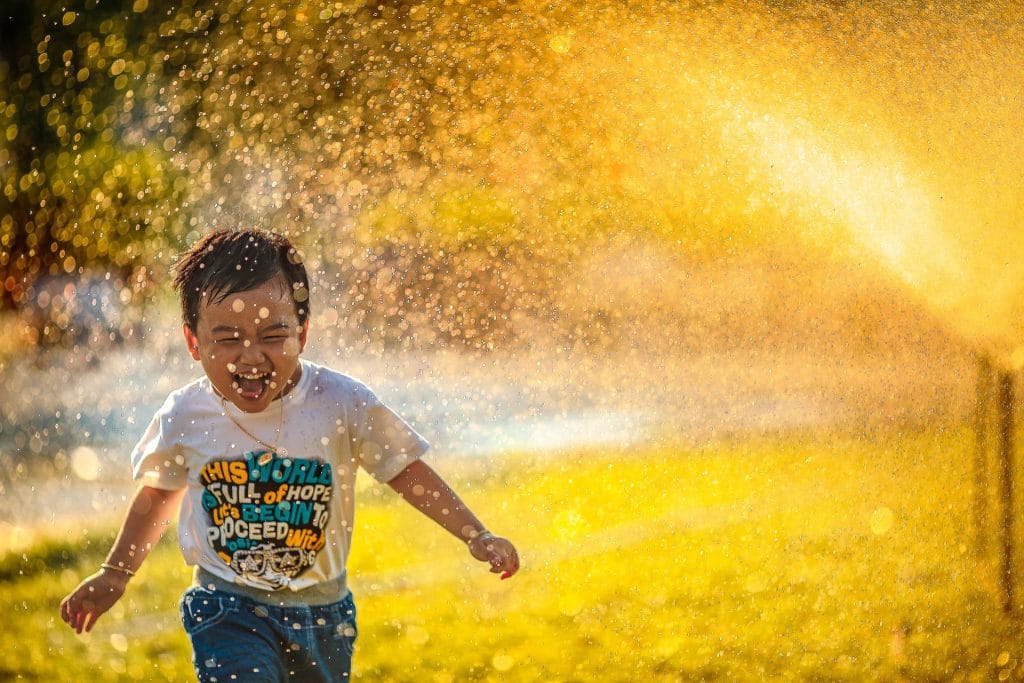 little boy running through a sprinkler