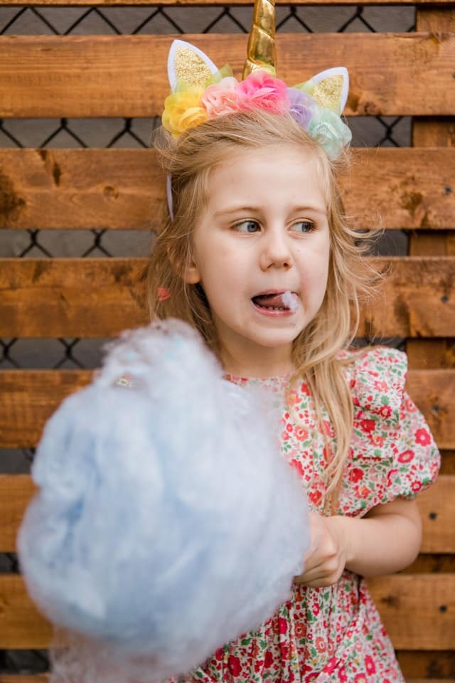 little girl dressed like a unicorn eating cotton candy